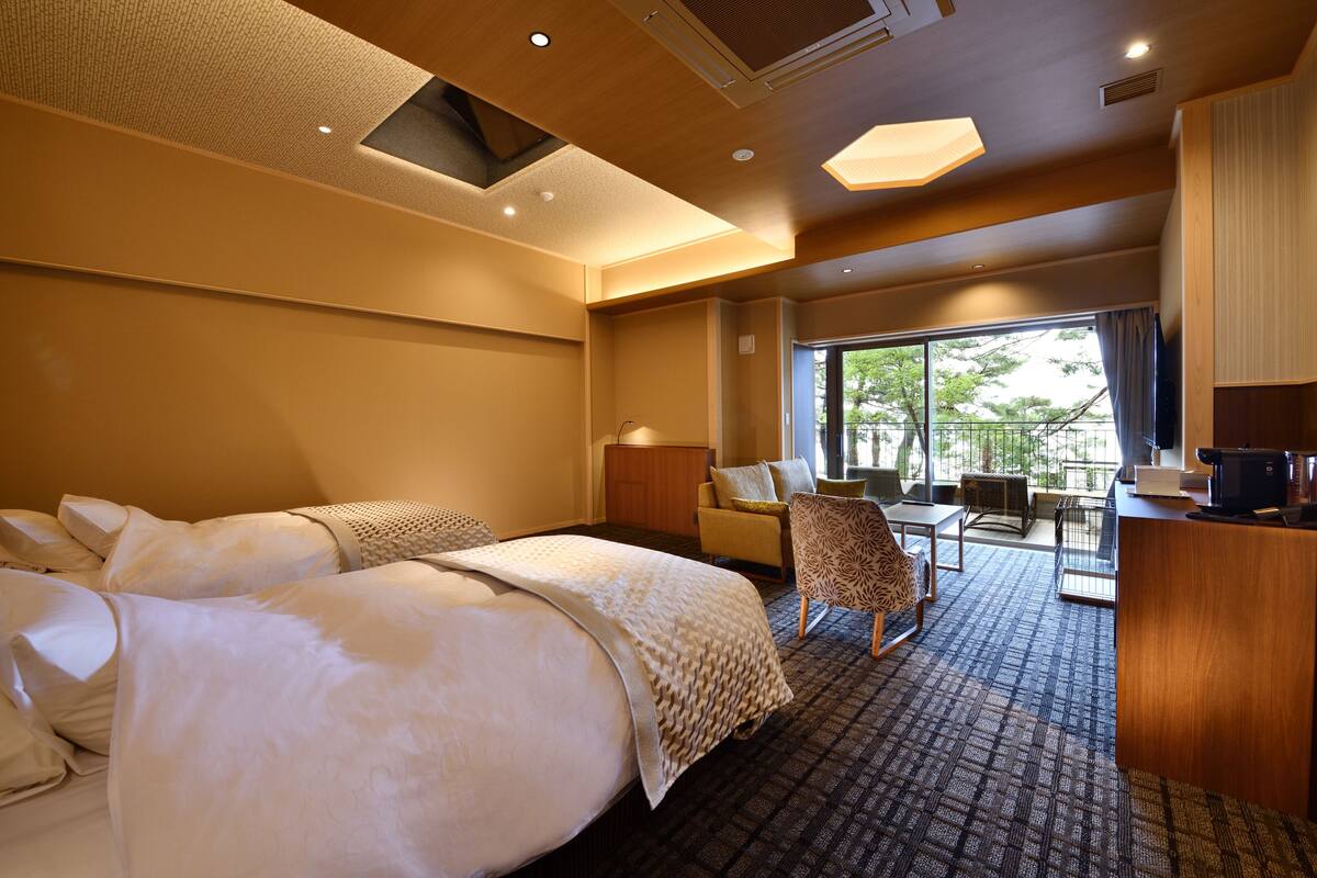 Ein Hotelzimmer mit einem großen Bett, einem Schreibtisch, einem Stuhl und Blick ins Freie.