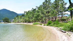 A beach with clear water, surrounded by trees and a mountain in the background. - Biwako Mastunoura Bettei (Otsu)