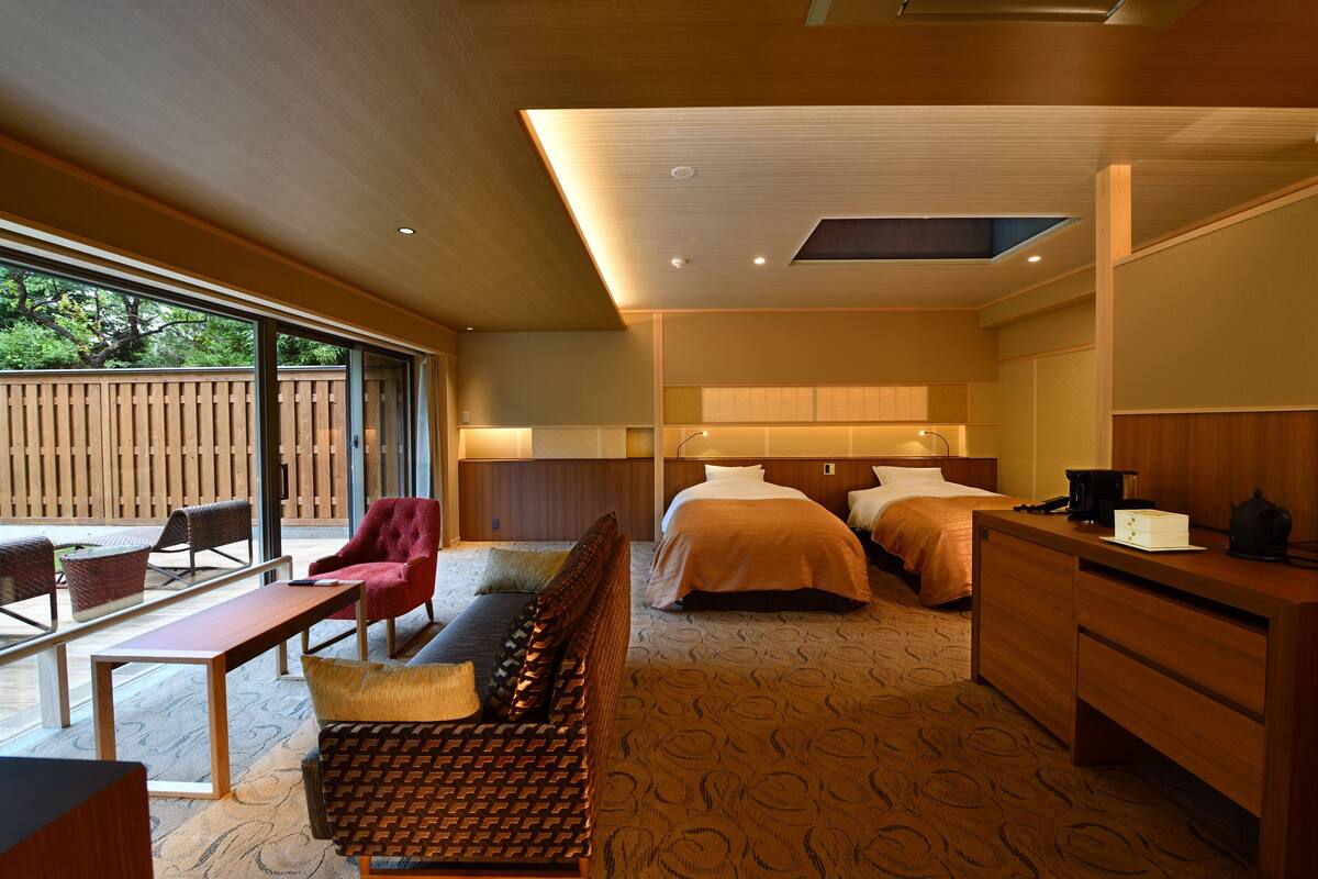 Ein modernes Hotelzimmer mit einem großen Bett, einem Schreibtisch, einer Sitzecke und Blick ins Freie.