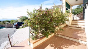 A residential property with a paved driveway, a staircase leading to a covered porch, and a view of the sea in the background. - BOUGAINVILLEA PRIMO PIANO (Marciana)