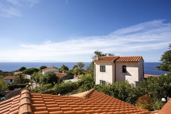 A coastal residential area with terracotta-tiled roofs, a small building with a white facade, and a clear view of the sea. - BOUGAINVILLEA PRIMO PIANO (Marciana)