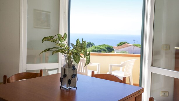 A room with a wooden table, a glass vase with a plant, and a view of the sea through large windows. - BOUGAINVILLEA PRIMO PIANO (Marciana)