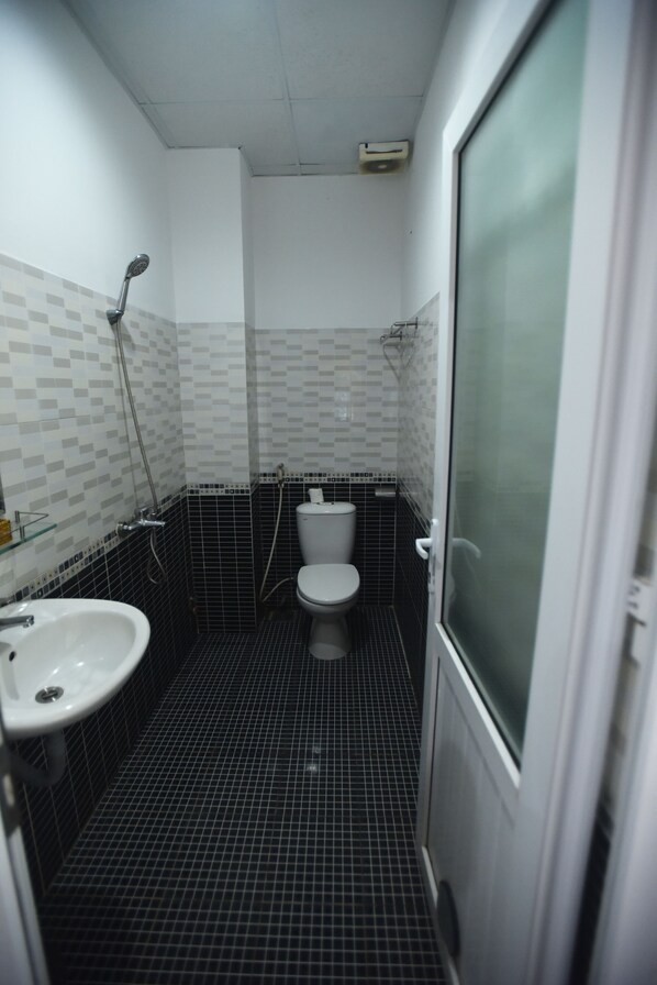 A small, tiled bathroom with a toilet, sink, and shower.