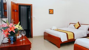 A hotel room with two beds, a wooden desk, a vase with flowers, and a picture on the wall.