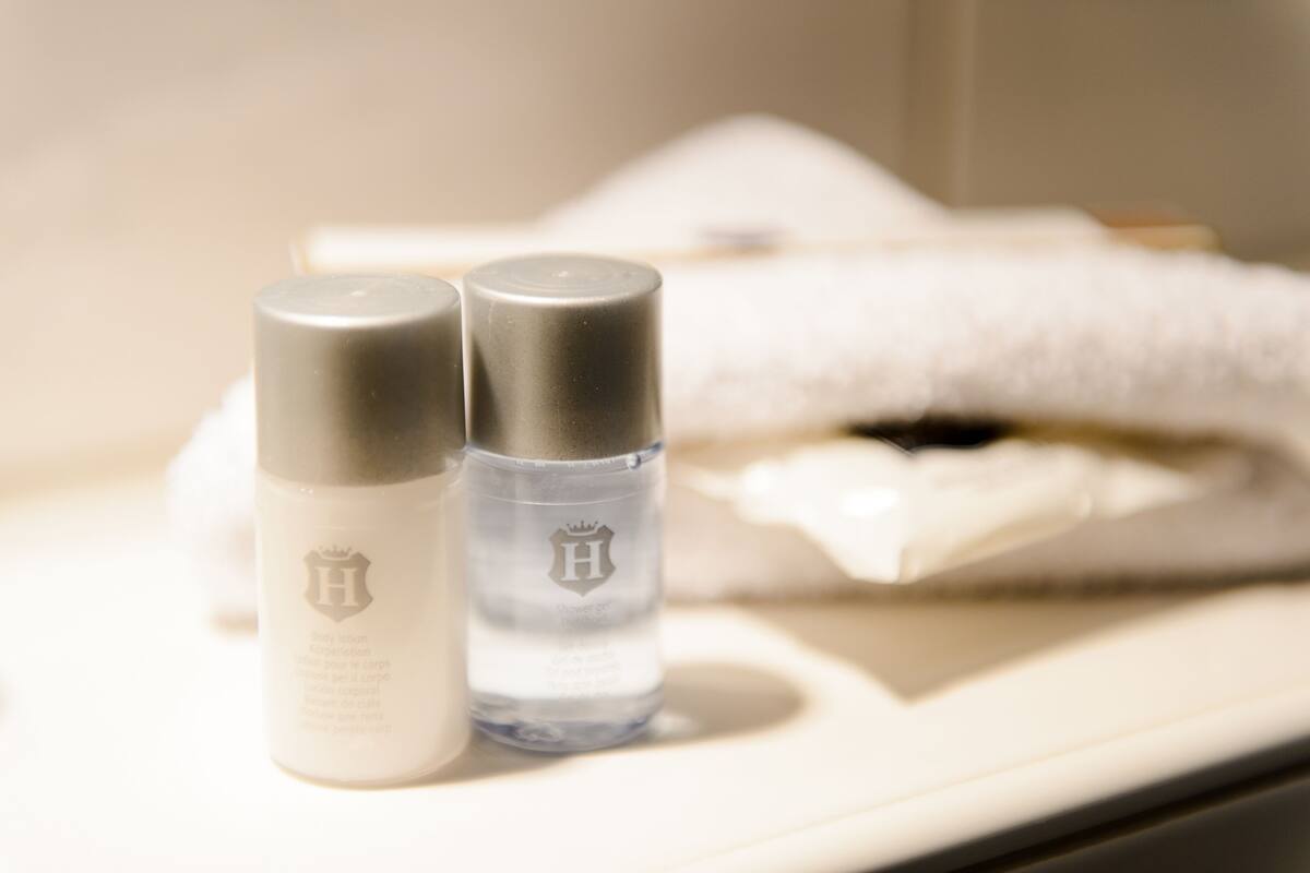 Two bottles of body lotion on a bathroom counter with a white towel in the background.