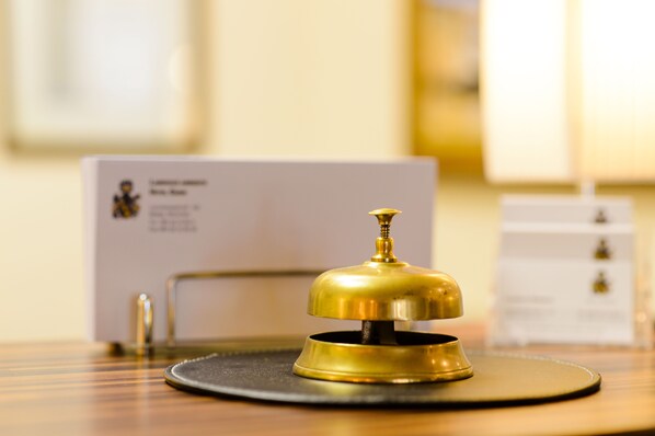 A brass bell on a black base, likely for room service, with a blurred background featuring a white sign with text.