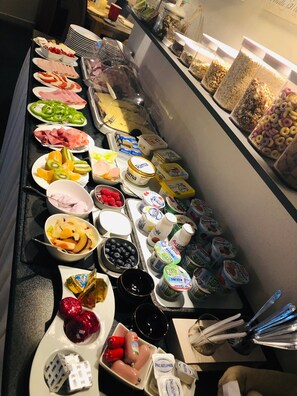 A buffet with various food items including fruits, cheeses, meats, and dairy products.