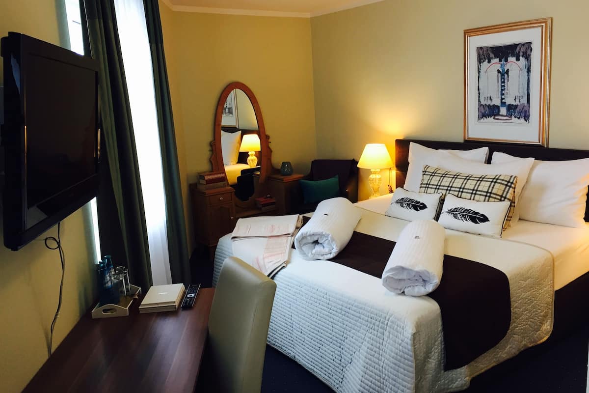 A hotel room with a bed, a television, a desk with a lamp, and a painting on the wall.