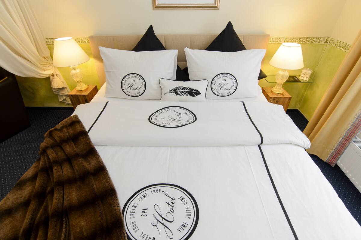 A neatly made bed with a white bedspread, black pillows, and a brown throw blanket. There are two bedside lamps on wooden nightstands.