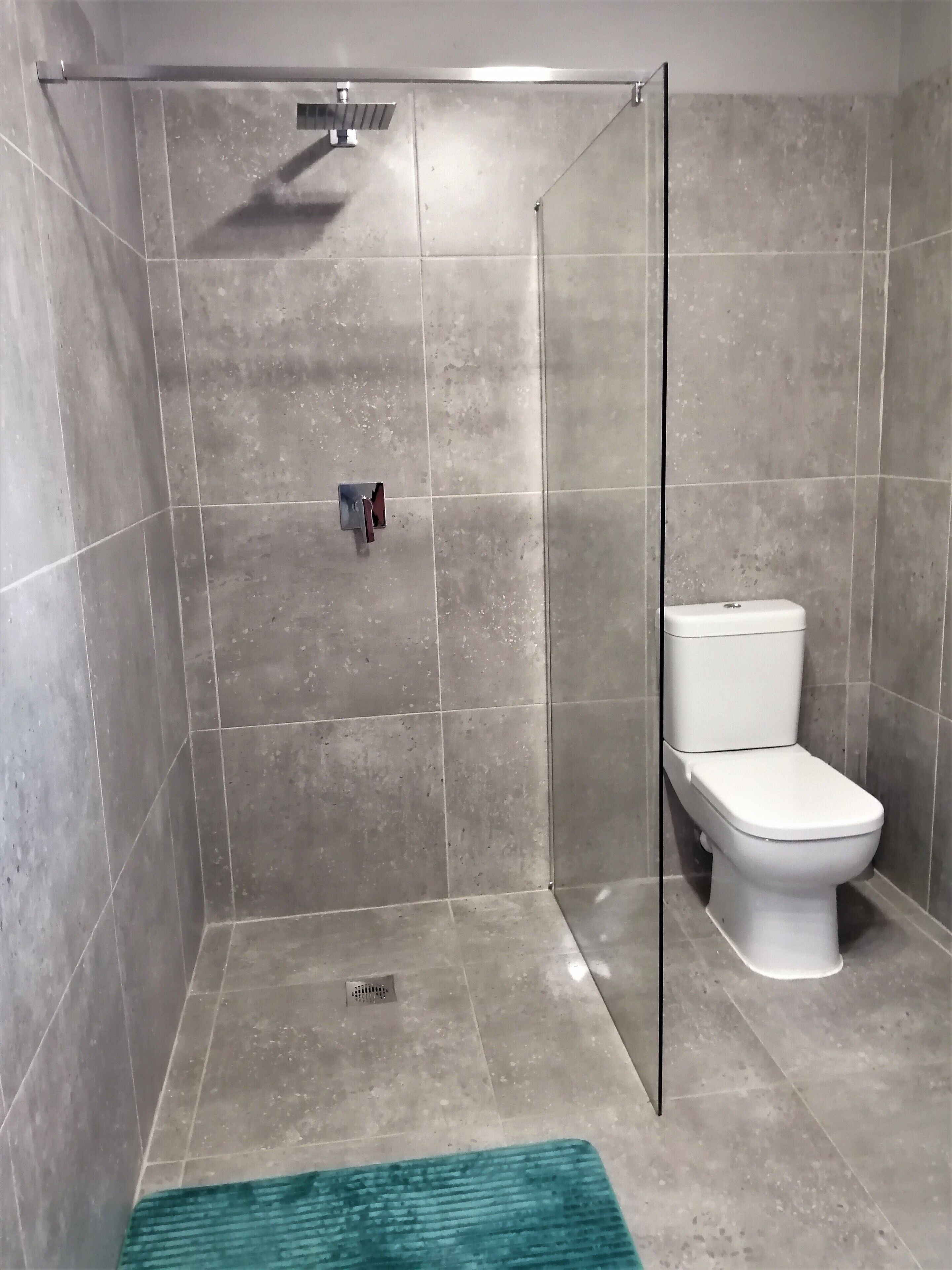 A modern bathroom with a shower enclosure, a toilet, and a visible drain.