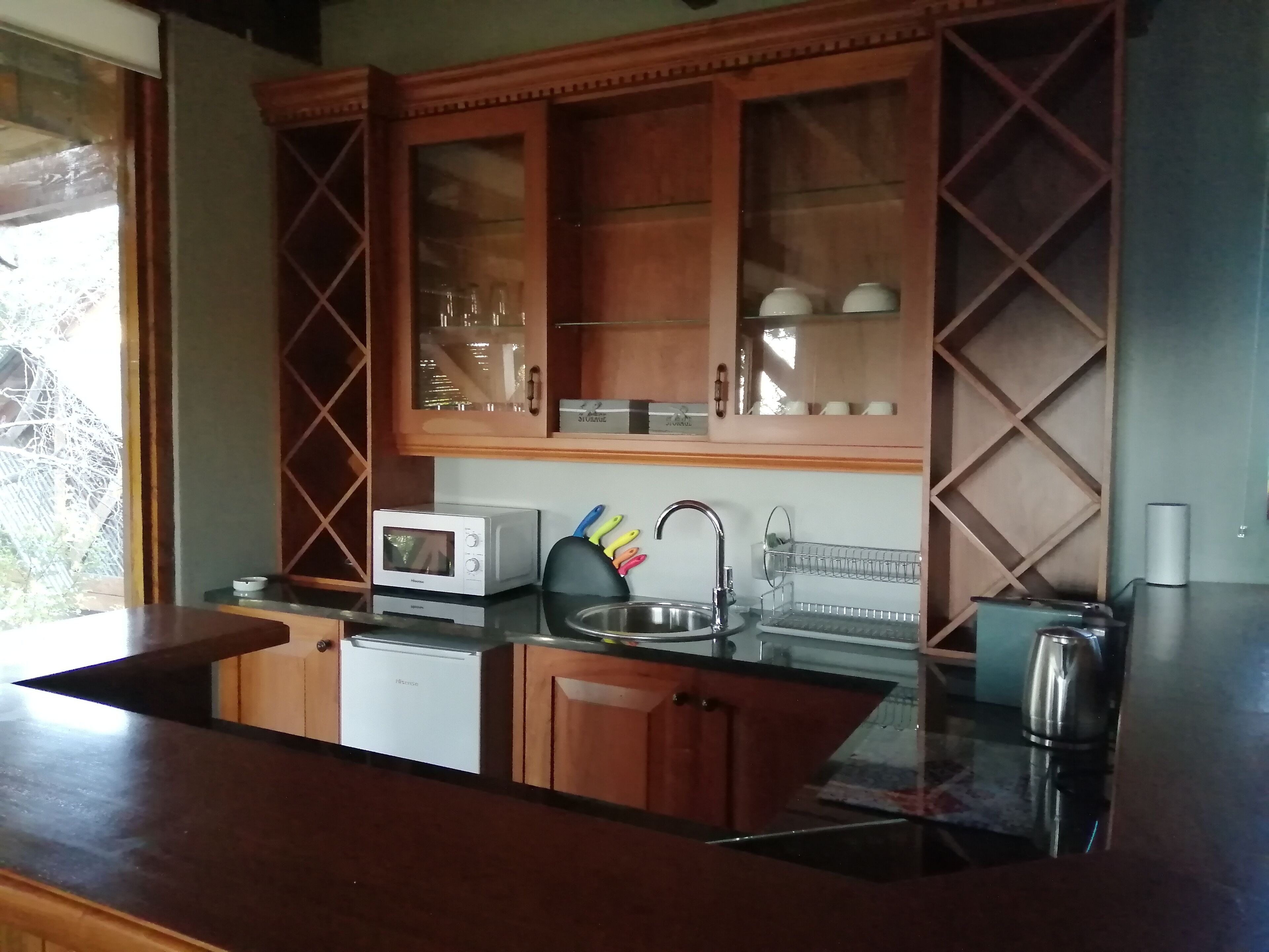 Una cocina con armarios de madera, microondas, tostadora, pileta y tetera.