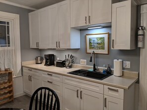 Compact kitchen area with sink, coffee maker, and toaster, plus cabinets and a framed picture.