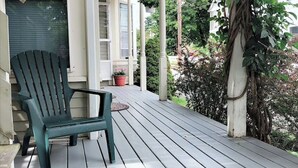 Una terraza de madera con una silla Adirondack verde y una alfombra pequeña.