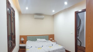 A bedroom with a bed, bedside table, lamp, and an air conditioning unit. - Quang Anh Hotel (Hanoi)