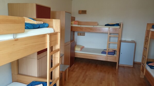 Une chambre de dortoir avec des lits superposés, des meubles en bois et un petit placard.