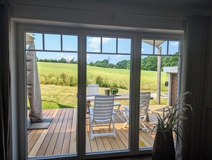 A room with a sliding glass door leading to an outdoor deck with wooden flooring, white chairs, and a table. - Apartment (56 m²) in the metropolitan region of Hamburg and yet idyllically located (Reinbek)