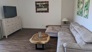 Una sala de estar con una mesa de centro de madera, un sofá, un televisor sobre un aparador y obras de arte en las paredes.