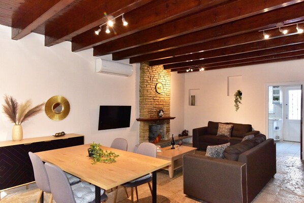 A modern living room with a wooden dining table, grey upholstered chairs, a brown sofa, and a stone fireplace.