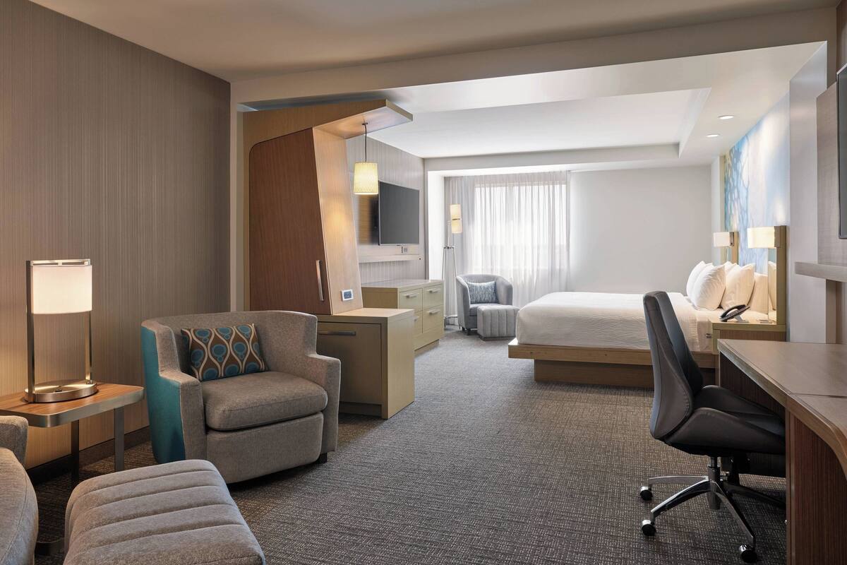 A hotel room with a bed, a desk, a chair, a TV, and a lamp.