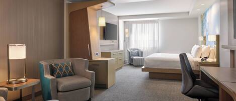 A hotel room with a bed, a desk, a chair, a TV, and a lamp.