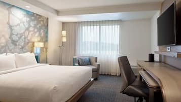 A hotel room with a large bed, a desk, a chair, a TV, and a window with curtains.