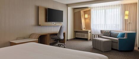 A hotel room with a large bed, a desk with a chair, a sofa, a television, and a window with curtains.
