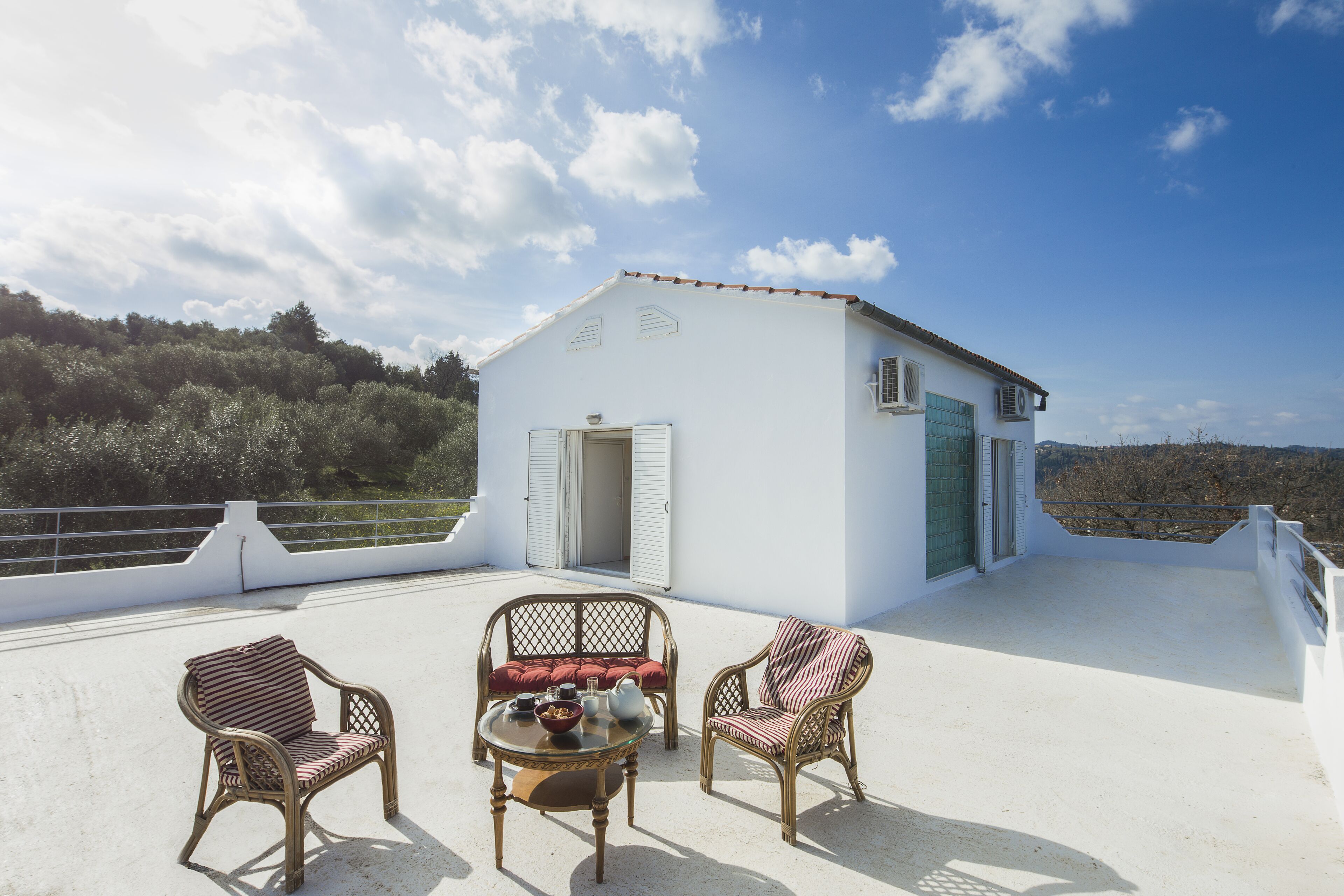 Terraza en la azotea con muebles de mimbre y una pequeña mesa, con vistas a un paisaje pintoresco.
