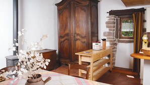 Ein Zimmer mit einem Holzschrank, einem Holztisch mit einer Bank, einer Vase mit weißen Blumen und einem Fenster mit Vorhang.