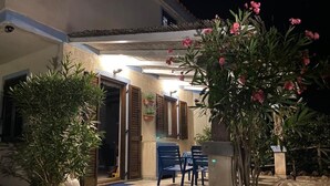 Un'area esterna ben illuminata con pavimento in pietra, piante in vaso e sedie blu.