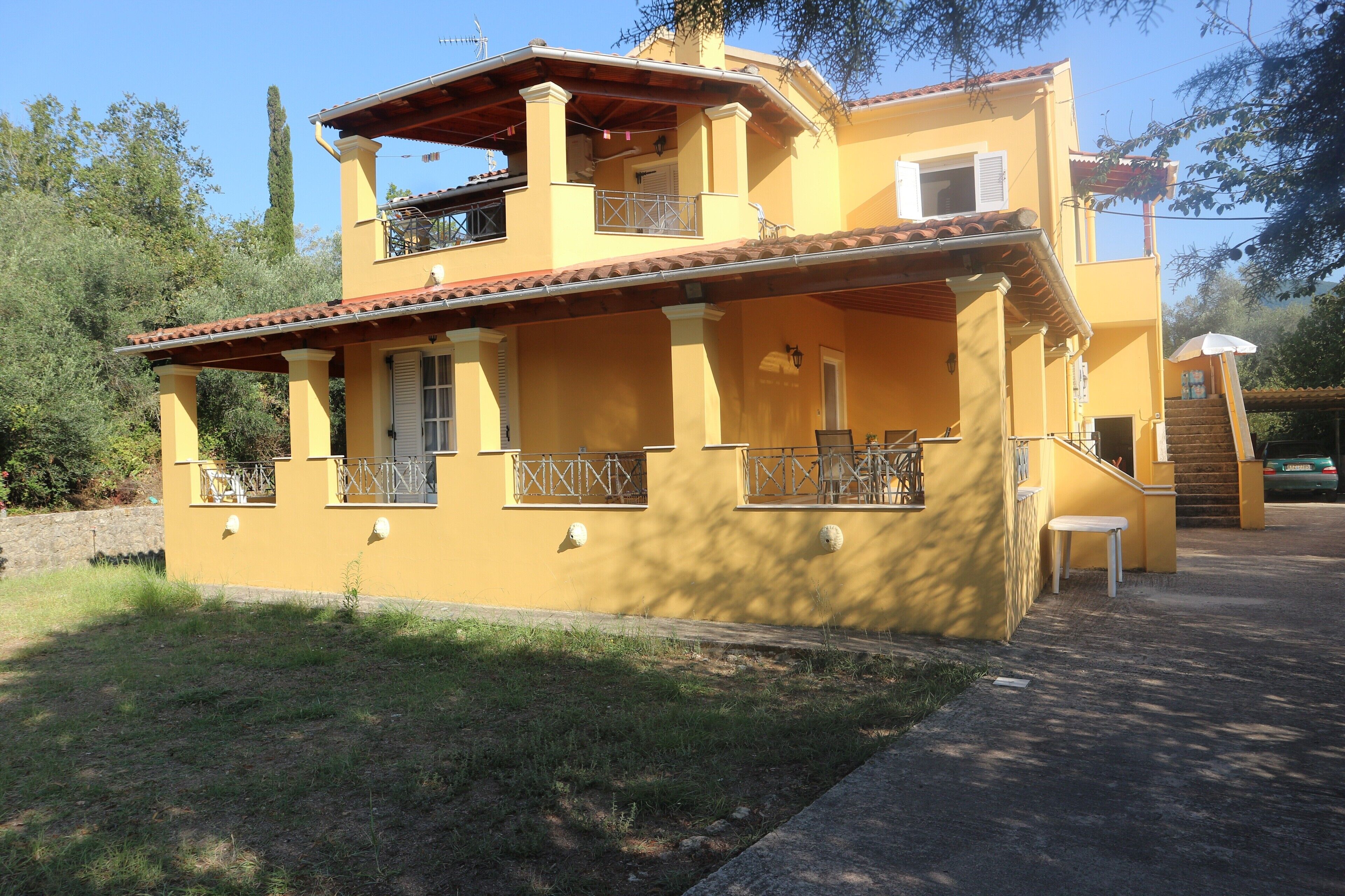 A two-story yellow building with balconies, a covered patio, and a staircase leading to an upper level.