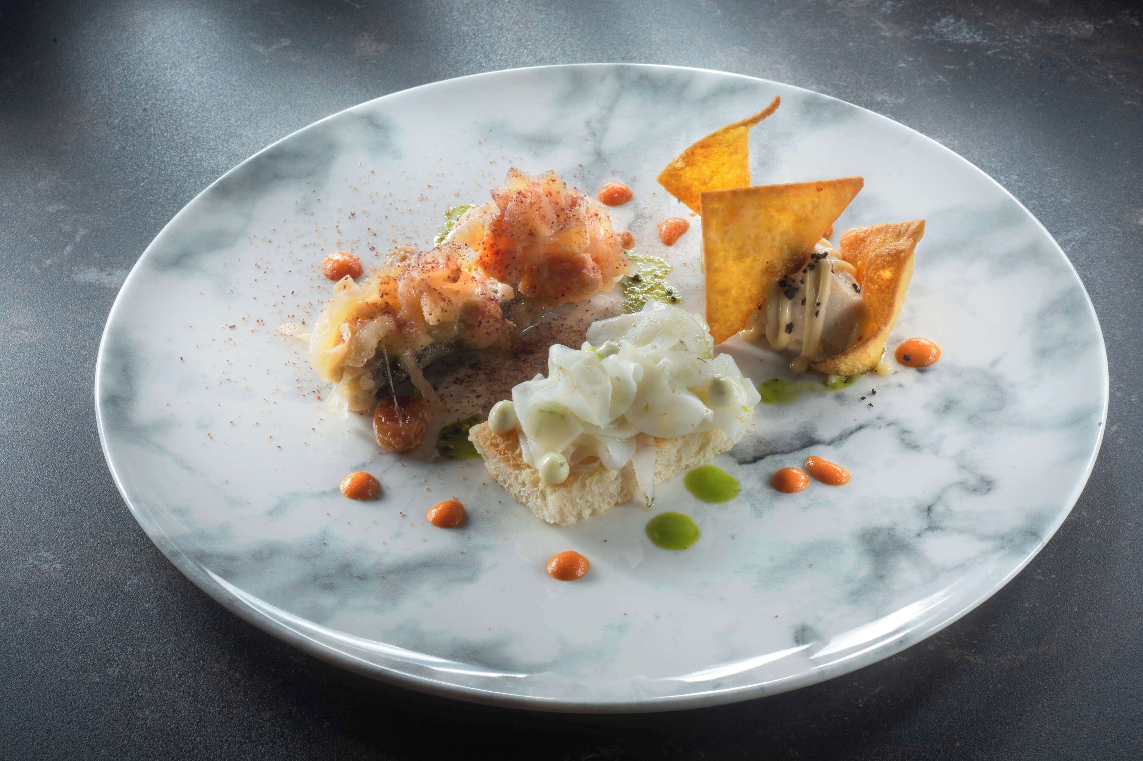 Un plato con diversos alimentos, como un trozo de pan, una cucharada de crema y algunos adornos.