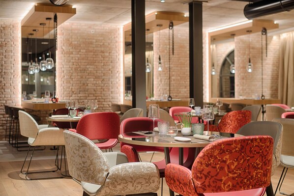 A restaurant interior with brick walls, hanging light fixtures, and a mix of red and beige chairs. - NH Collection Venezia Murano Villa (Venice)