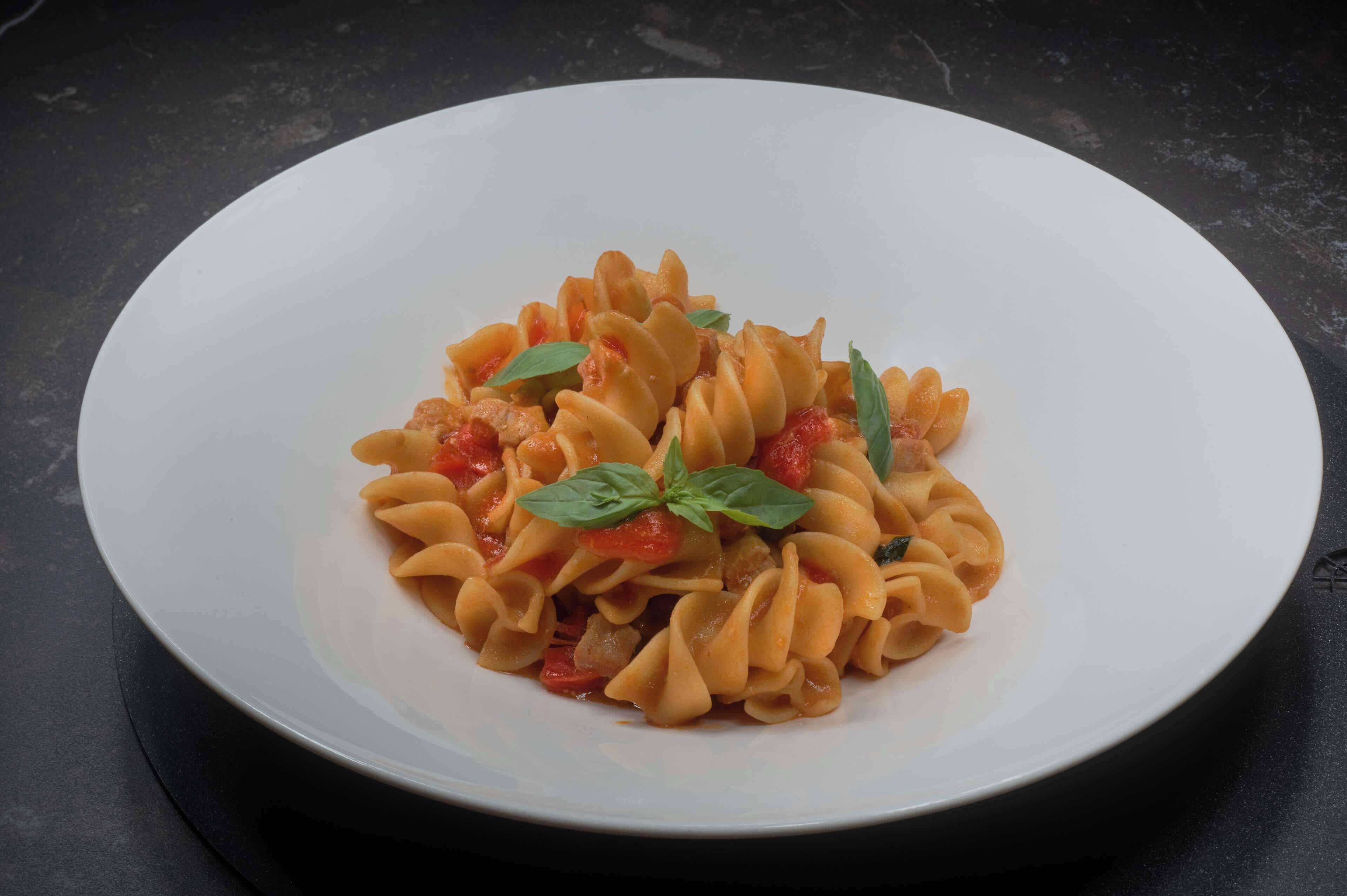 A white plate with pasta, tomatoes, and basil on a dark surface.