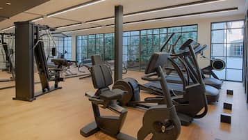 Ein Fitnessraum mit verschiedenen Trainingsgeräten, großen Fenstern und Holzboden.