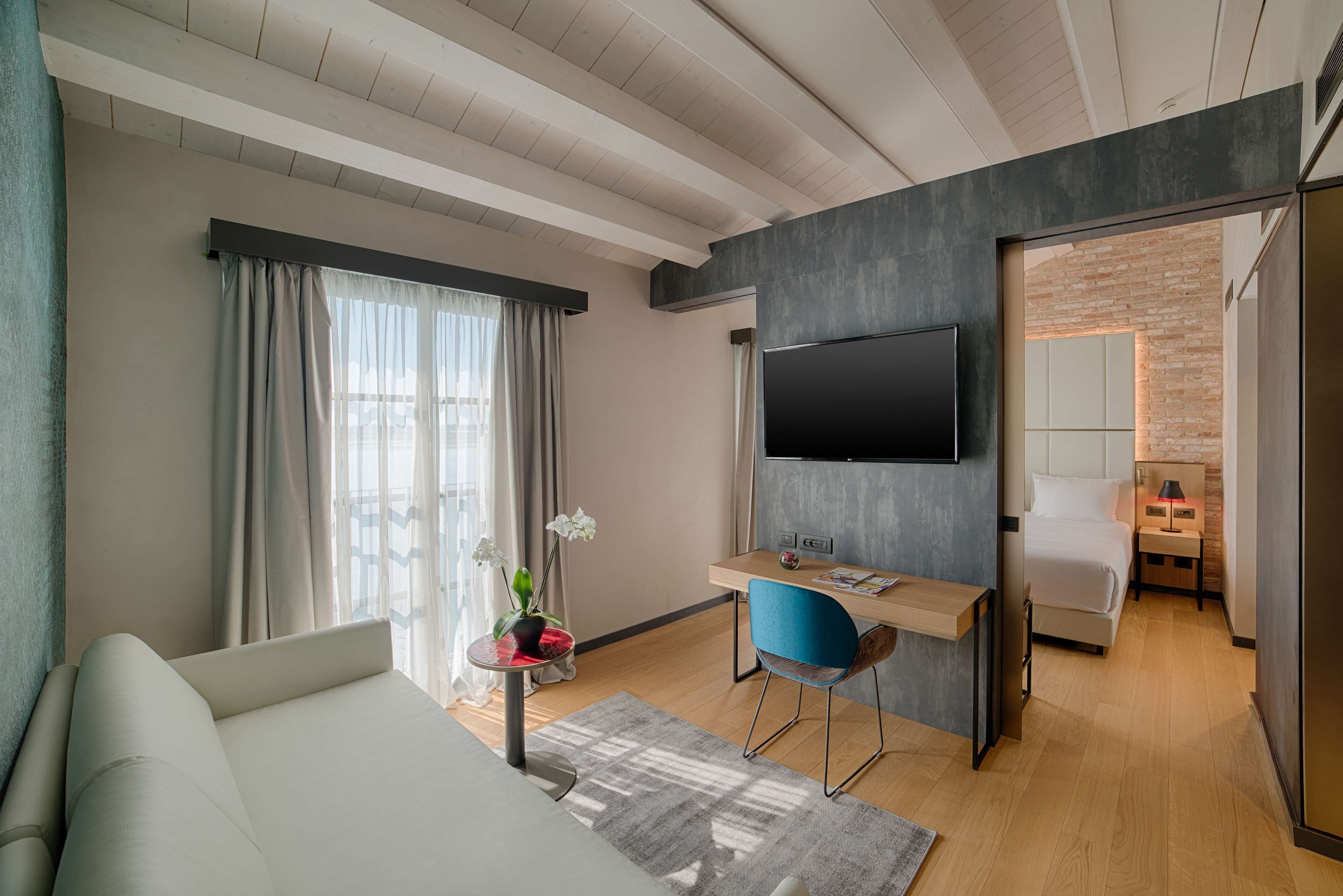 Una habitación de hotel moderna con una cama, un escritorio con una silla, un televisor y una pequeña mesa con una planta.