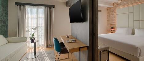 A modern hotel room with a bed, a desk with a chair, a TV mounted on the wall, and a window with curtains.