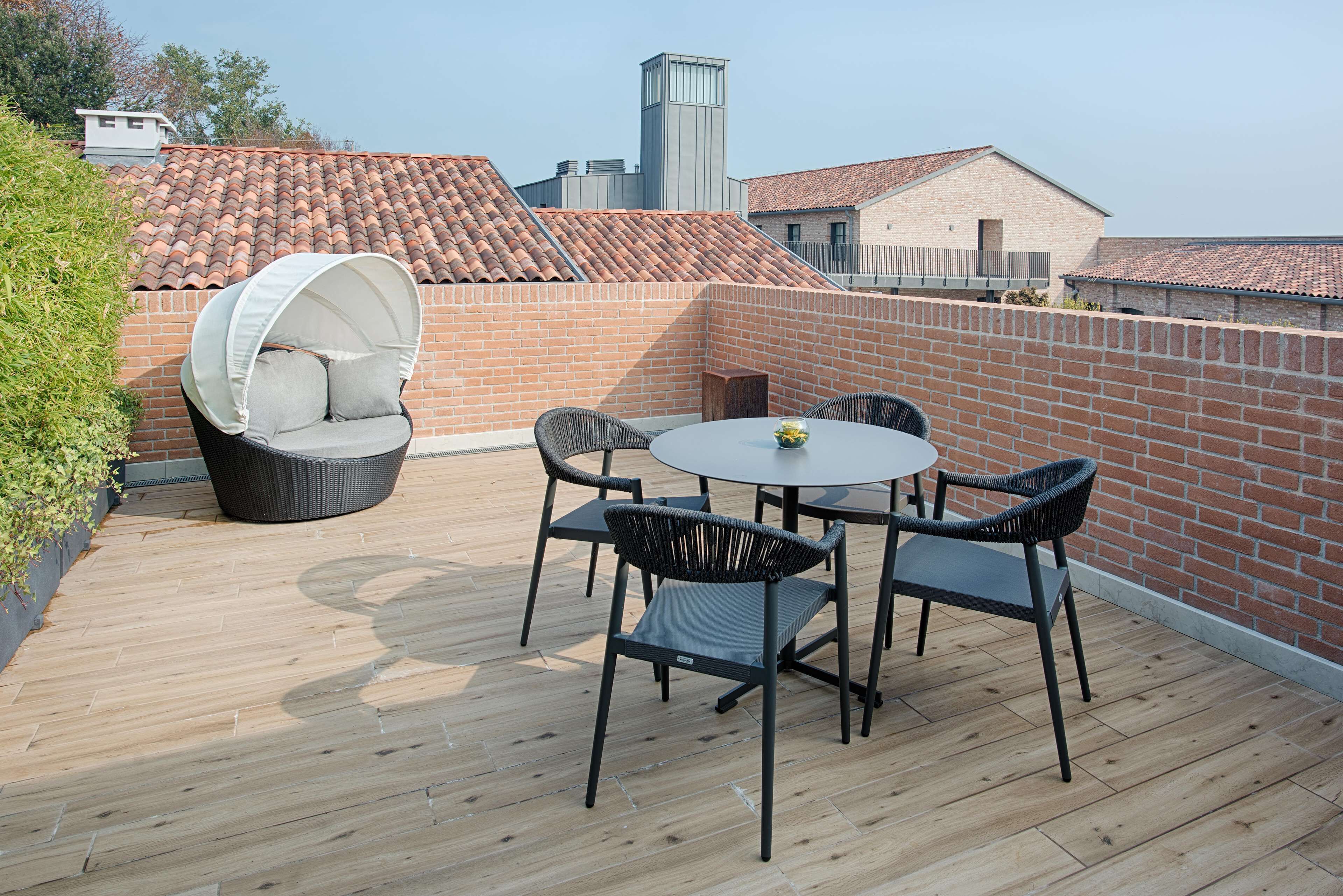 Een terras op het dak met een ronde tafel en vier stoelen, omgeven door een bakstenen muur en een houten terras.