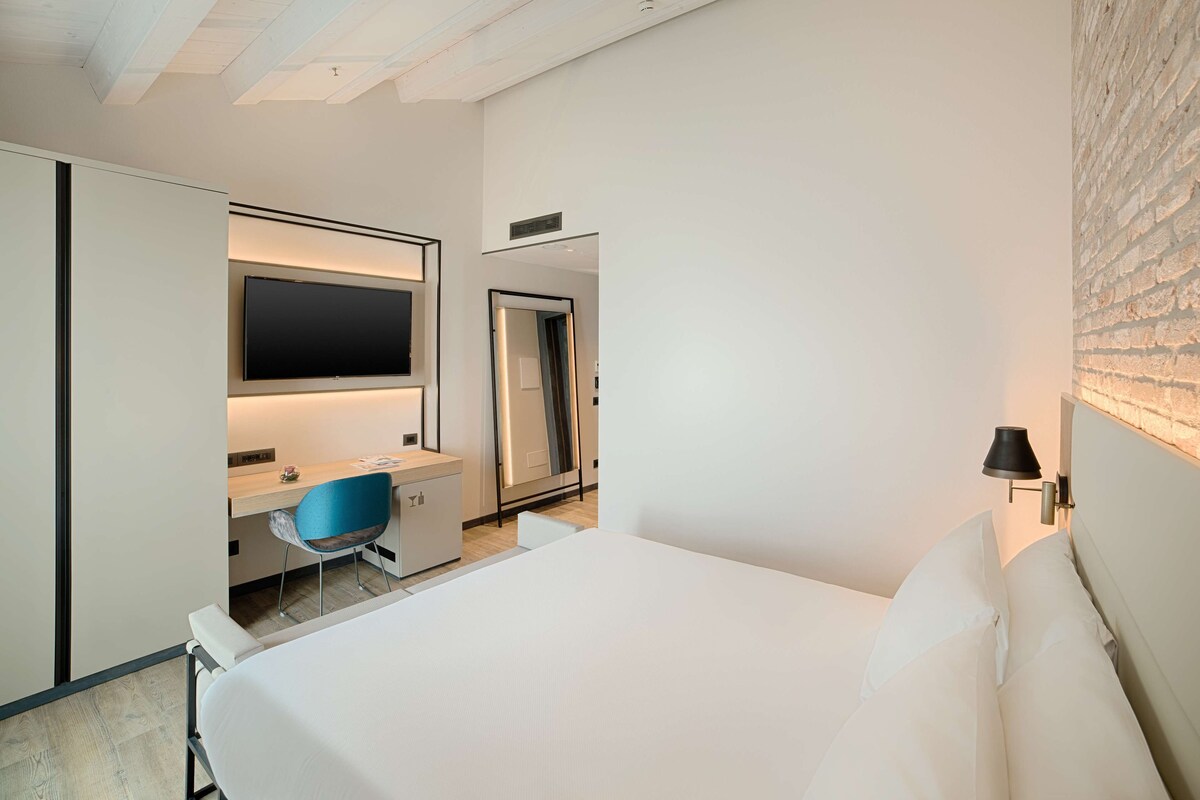 A hotel room with a bed, a desk with a chair, a TV, and a mirror.