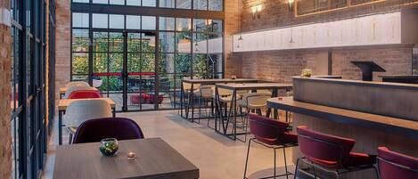 A modern restaurant with large windows, brick walls, and a mix of red and white chairs.