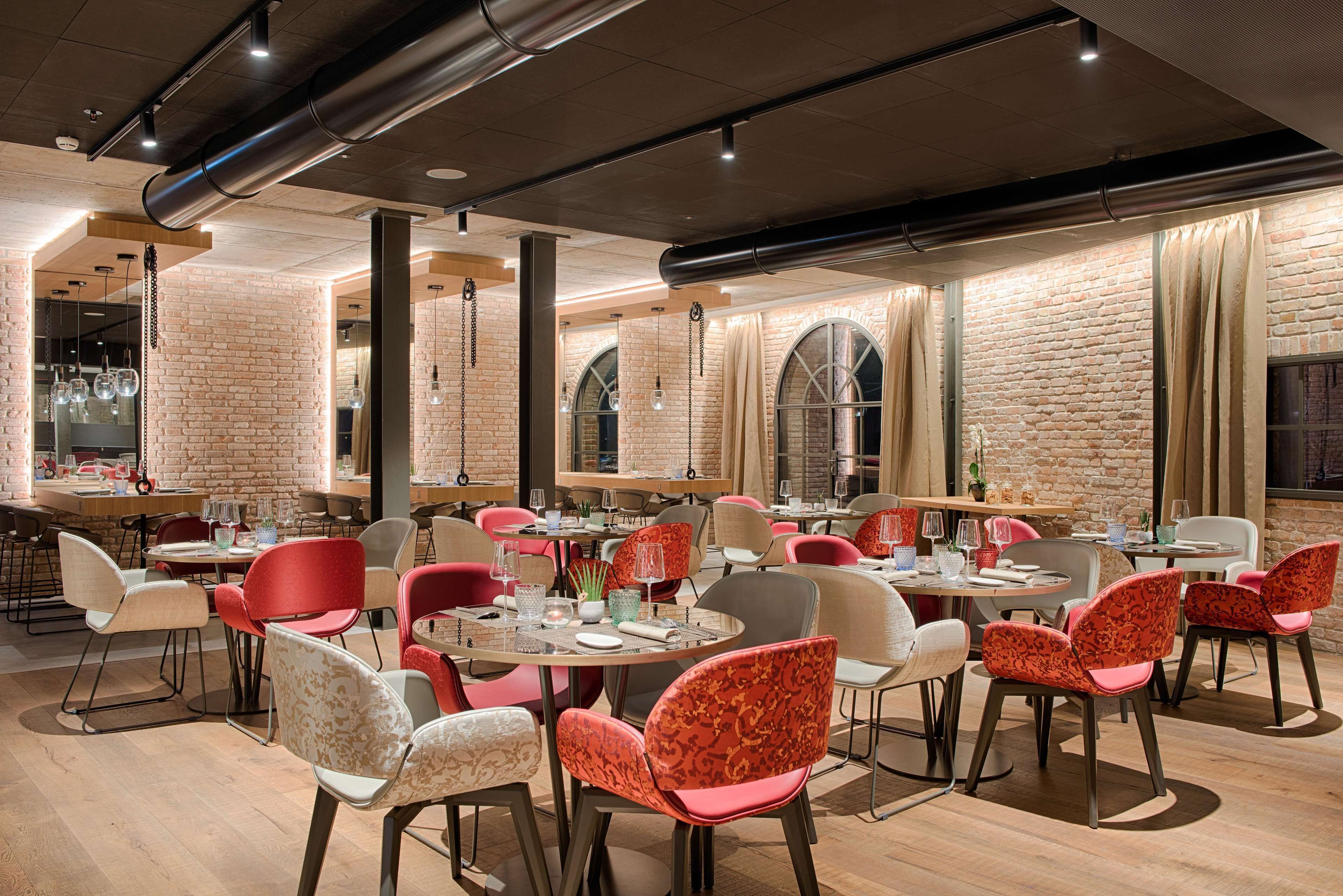 Ein modernes Restaurant mit Ziegelwänden, runden Tischen und einer Mischung aus roten und weißen Stühlen.
