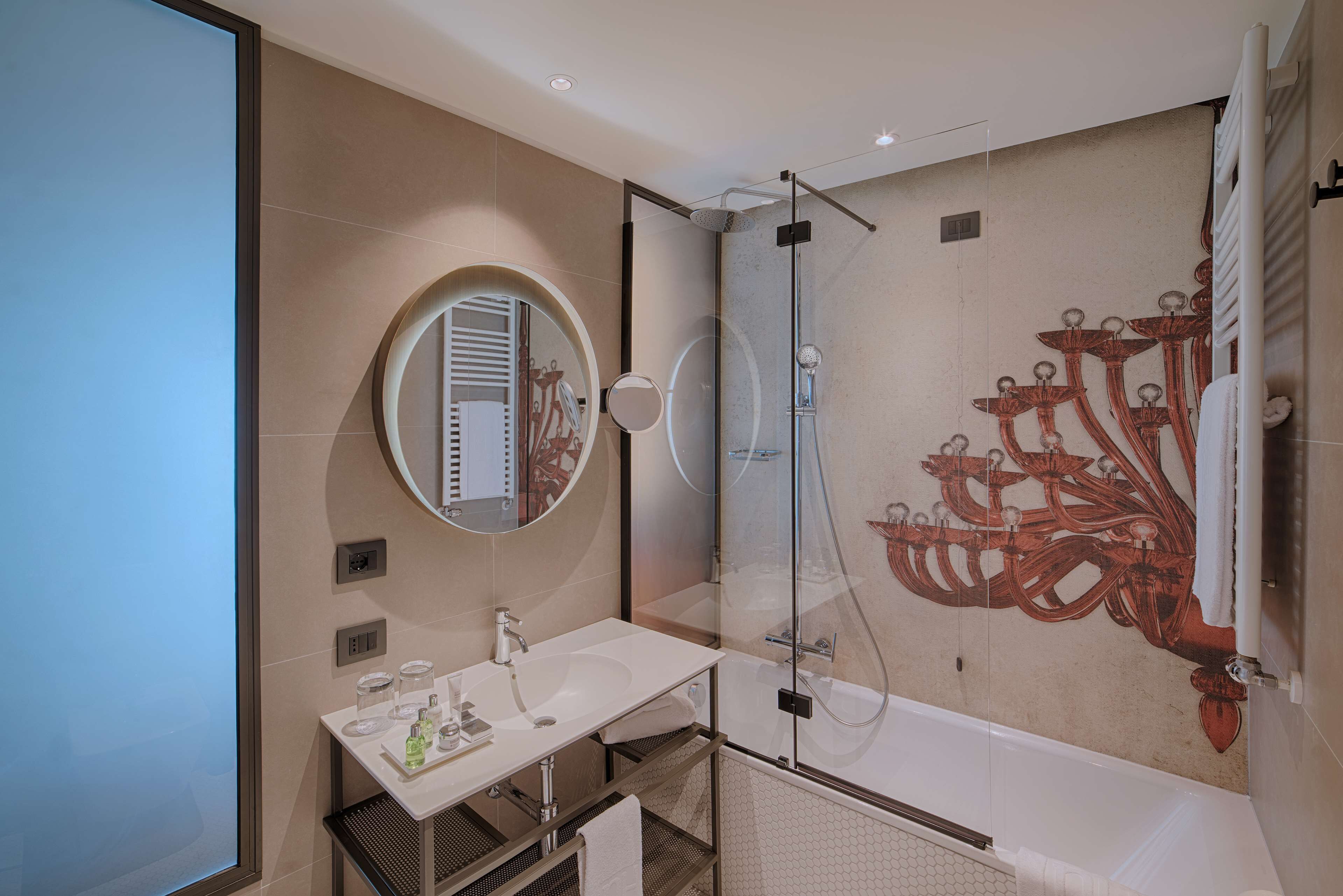 A modern bathroom with a glass-enclosed shower, a round mirror, and a white sink.