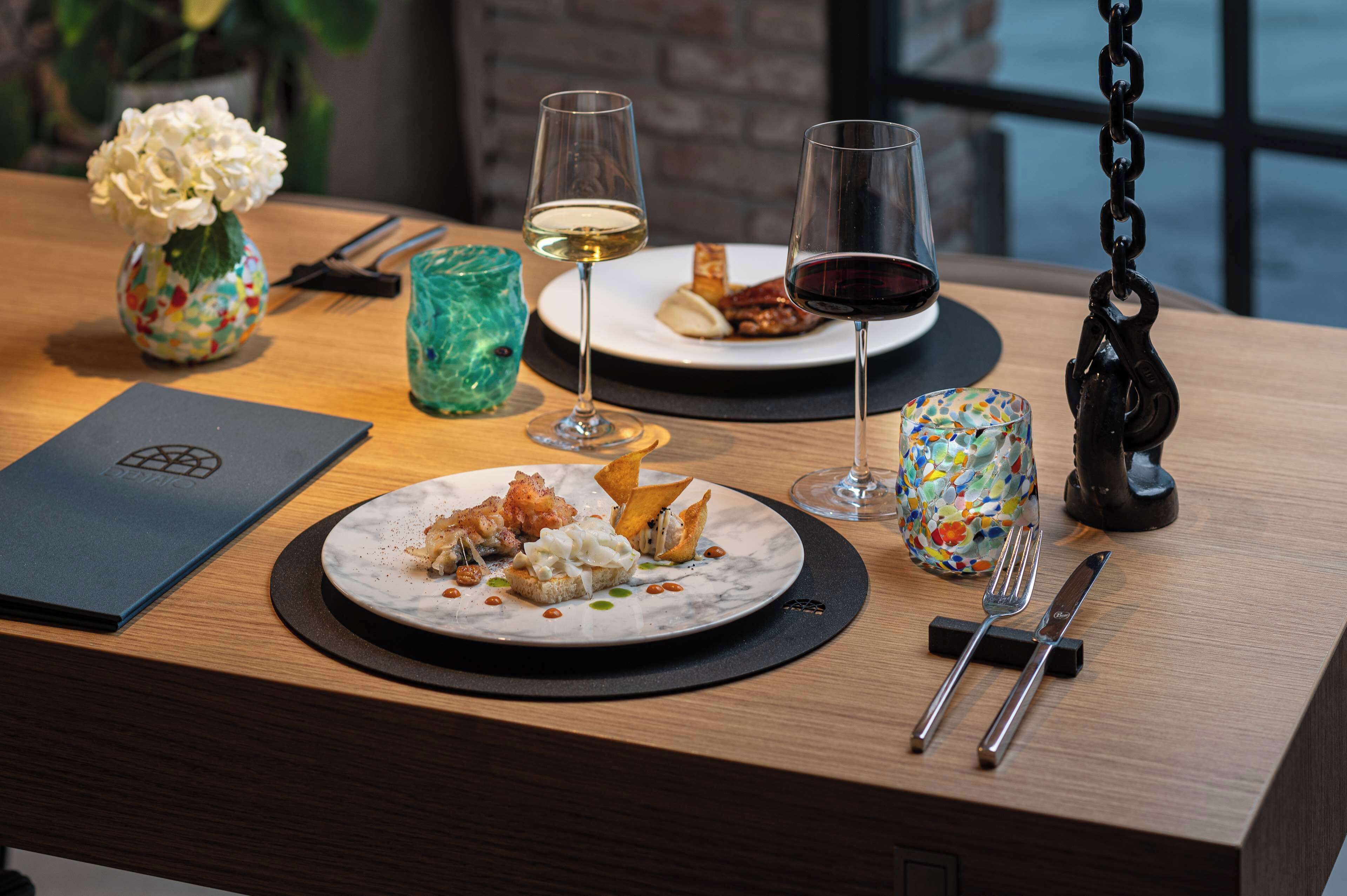 Una mesa de comedor con platos de comida, copas de vino y cubiertos.