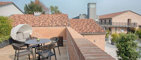 A rooftop patio with a brick wall, a round table with chairs, and a small garden area.