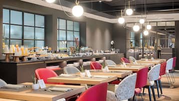 Ein moderner Essbereich mit mehreren Tischen und Stühlen, eine Buffettheke mit verschiedenen Speisen und große Fenster, die natürliches Licht hereinlassen.