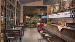 A modern bar area with a brick wall, glass doors leading to a garden, and a variety of seating options including tables and chairs. - NH Collection Venezia Murano Villa (Venice)