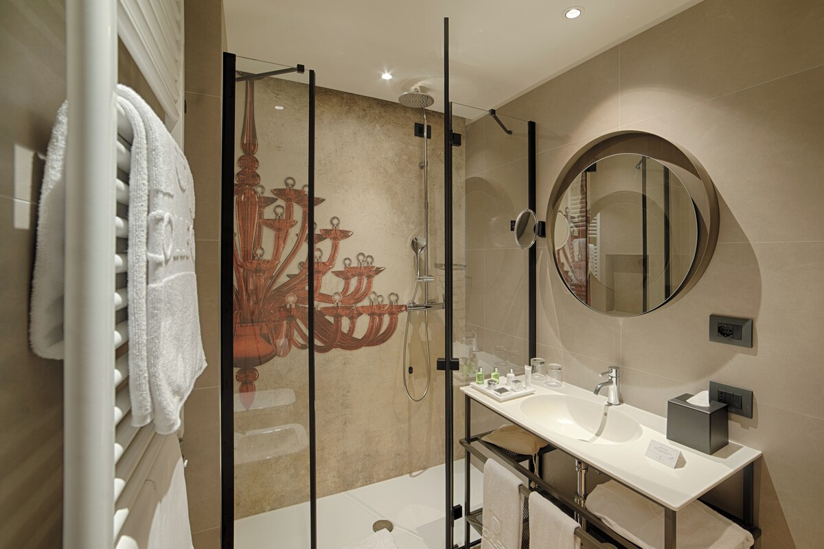 Un baño moderno con cabina de ducha de vidrio, un espejo redondo y un lavabo blanco.