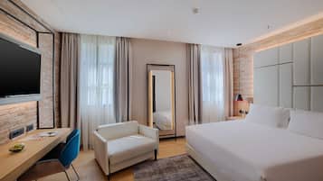 Quarto de hotel moderno com uma cama grande, uma escrivaninha com cadeira, televisão de tela plana e um espelho amplo.