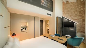 Ein modernes Hotelzimmer mit einem großen Bett, einem Schreibtisch, einem Stuhl, einem Fernseher und einer Küchenzeile.