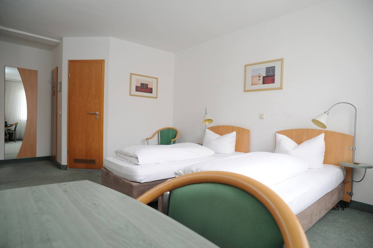 A hotel room with a bed, a chair, a desk, and a lamp.