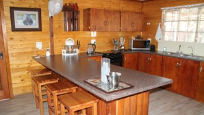 Une cuisine rustique aménagée dans une cabane en bois, avec un plan de travail en granit, des tabourets en bois, un four à micro-ondes et un évier.
